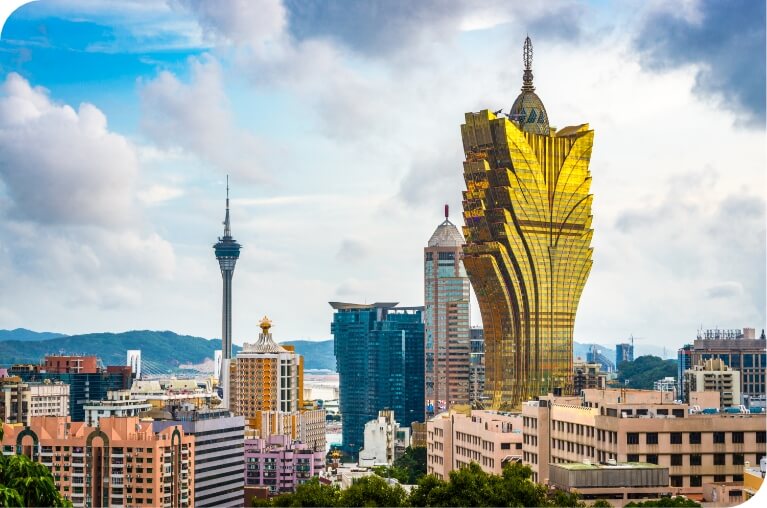 A skyline view of a modern city featuring a golden, uniquely shaped skyscraper and surrounding buildings, with a cloudy sky and distant mountains in the background.