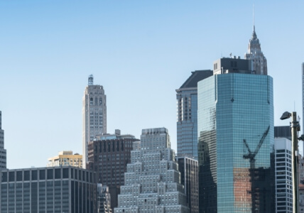 Skyline of a modern city featuring a variety of tall skyscrapers, including glass buildings reflecting the sky, with clear blue skies in the background.