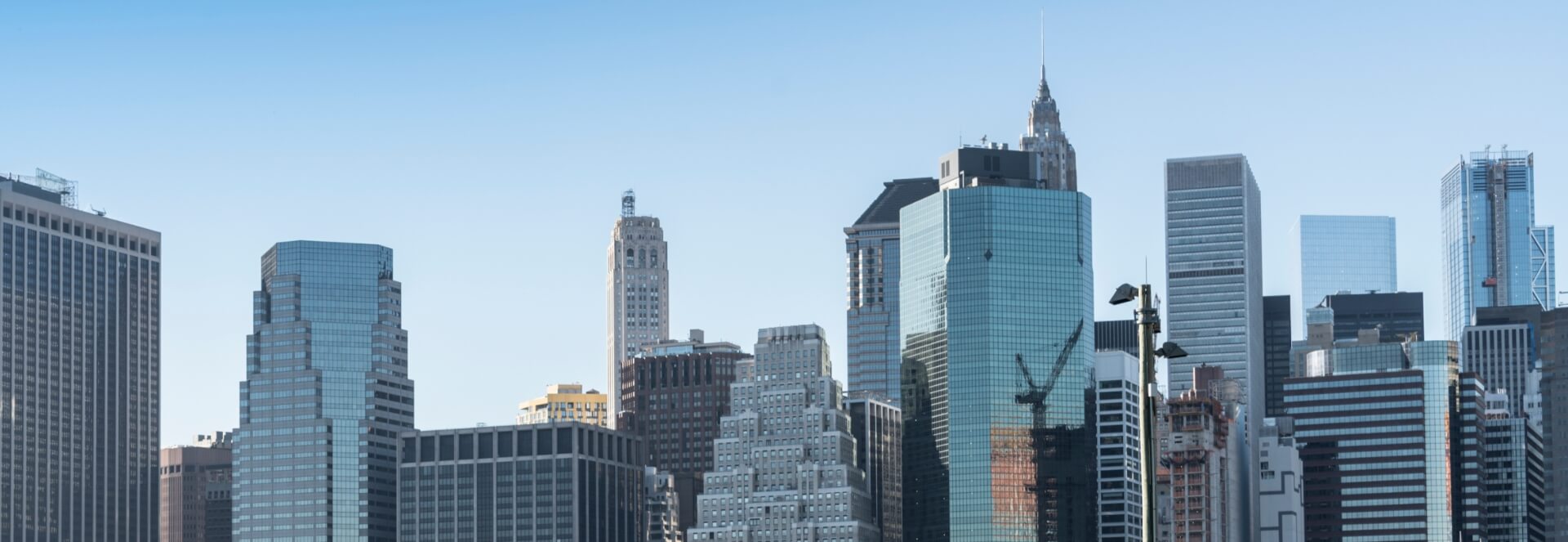 Skyline of a modern city featuring a variety of tall skyscrapers, including glass buildings reflecting the sky, with clear blue skies in the background.