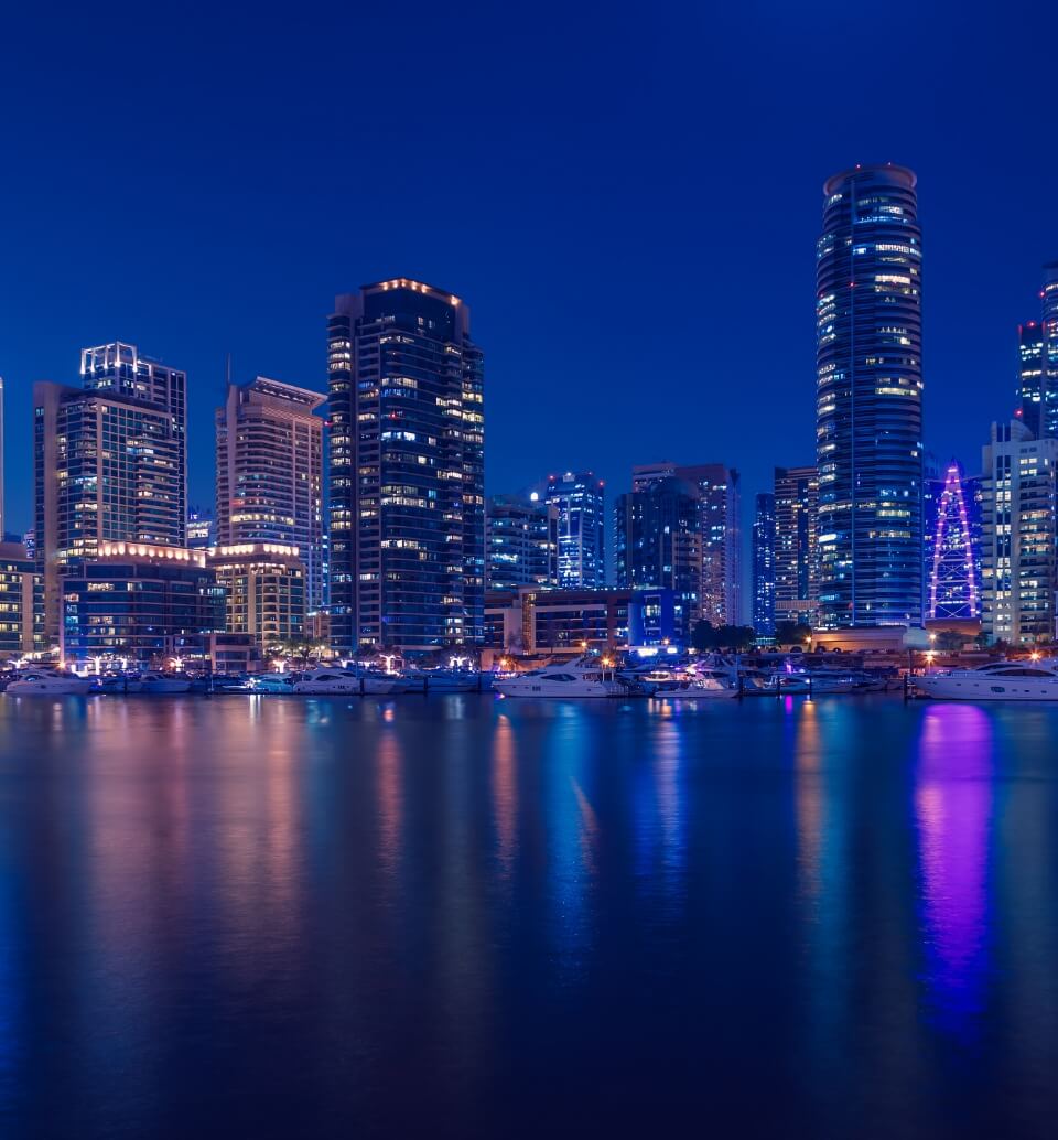 A stunning night view of a modern city skyline with skyscrapers reflecting in the water. The city is brightly lit, with lights reflecting in the water.